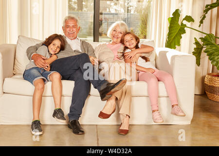 Glückliche Großeltern und zwei Enkelkinder sitzen auf einem Sofa in der Wohnung Stockfoto
