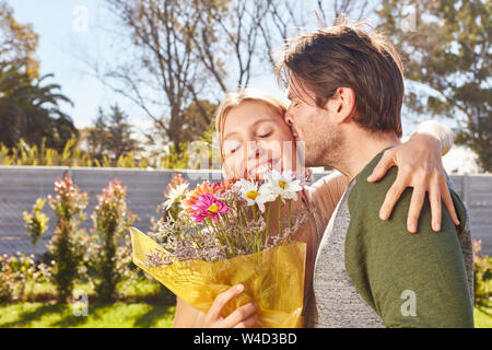 Mann küsst seine Freundin und gibt ihr einen Blumenstrauß willkommen Stockfoto