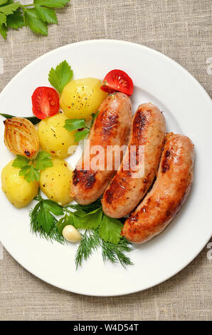 Gebratene Würstchen und Gemüse auf weiße Platte, Ansicht von oben Stockfoto