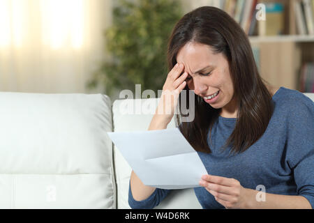 Traurige Frau mit einem Buchstaben auf einer Couch im Wohnzimmer zu Hause sitzen Stockfoto