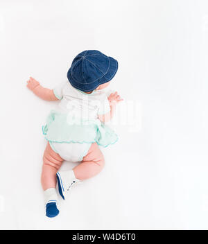 Crawling Baby auf weißem Hintergrund in Jeans Hut und Stiefeletten, Kleinkind Draufsicht, Neugeborenes Kind auf Decke Stockfoto