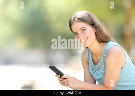 Happy woman holding Smartphone mit Kamera in einem Park einen sonnigen Tag sitzen Stockfoto