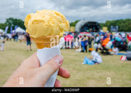 Eine männliche Hand mit einem Kegel von Eis in ein Feld auf einem Festival. Stockfoto