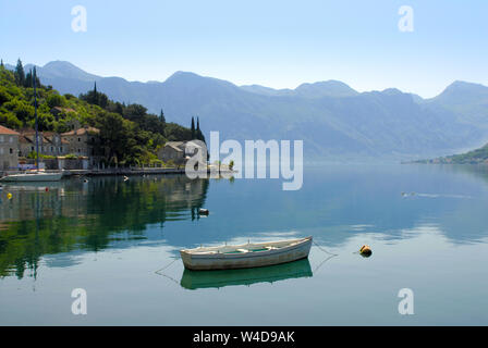 Boot auf einem noch Wasser gegen Berge und alte Häuser. Bucht von Kotor, Montenegro Stockfoto