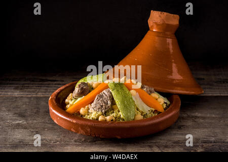 Traditionelle Tajine mit Gemüse, Kichererbsen, Fleisch und Couscous auf hölzernen Tisch. Stockfoto