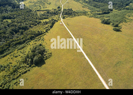 Luftaufnahmen mit einer Drohne. Gerade die unbefestigte Straße durch das Feld und Wald läuft. Stockfoto