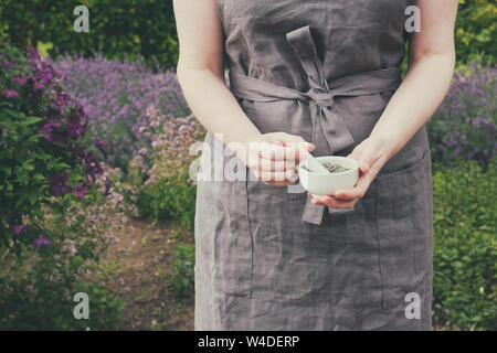 Frau in ihrer Hände halten ein Mörtel von heilenden Kräutern. Herbalist sammelt Heilpflanzen im Garten. Stockfoto