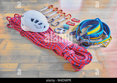 Kletterausrüstung auf hölzernen Hintergrund: rot dynamisches Seil mit blauen Streifen, Helm, blau/gelben Kabelbaum, Expressschlingen, Belay Device mit HMS Karabiner, Stockfoto