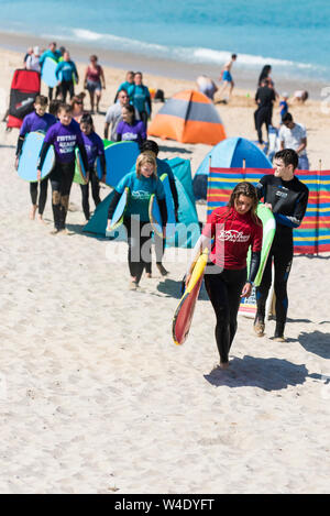 Eine Surf Instructor von den Fistral Beach Surf School führenden ihrer Klasse von Lernenden über Fistral Beach nach einer surflektion. Stockfoto