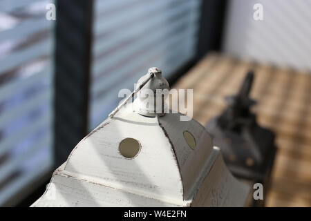 Weiße und braune Laternen auf einen Holzboden, der an einem sonnigen Tag. In Balkon mit gestreiften Glas Zaun schöne Schatten fotografiert. Nahaufnahme. Stockfoto