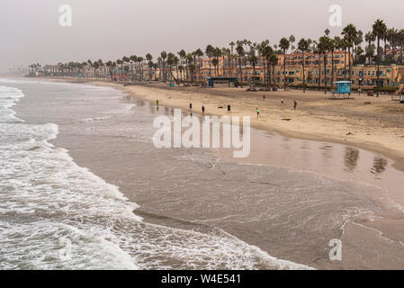 Blick nach unten an der Küste mit Wellen und Strand mit Ferienwohnungen, Apartments und Eigentumswohnungen entlang dem Strand mit hohen Palmen. Stockfoto