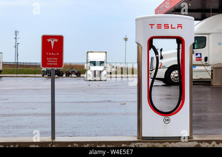 Tesla Kompressor Stall und "Tesla Elektroautos nur'-Schild mit truck-Stop im Hintergrund. Stockfoto