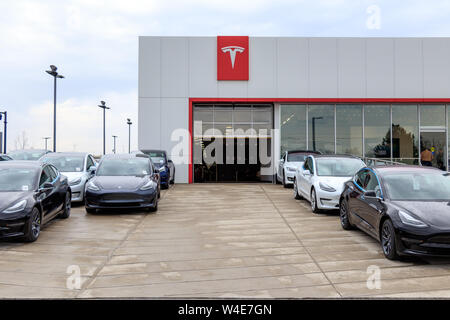 Tesla Logo ist bei Tesla Händler/Service Center mit Tesla Modell 3 ist die Lieferung warten auf - Rampe gesehen. Stockfoto