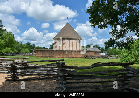 Das Colonial Williamsburg Powder Magazine gegen einen blauen Himmel mit Cottony weiße Wolken im Hintergrund und einer Split Schiene Zaun im Vordergrund. Stockfoto