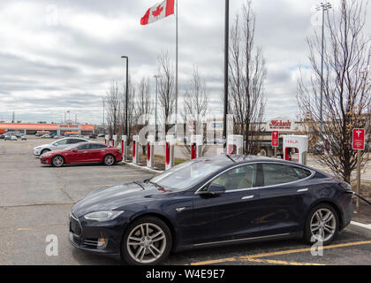 Blau Tesla Model S geparkt, Aufladung in Markham, mit Model S, Modell X und Kanadischen Flagge schwenkten im Hintergrund. Stockfoto