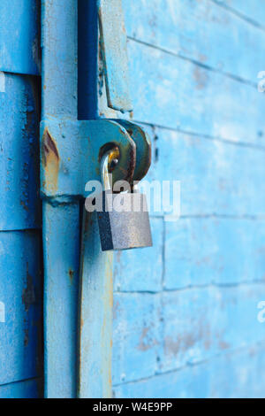 Alte Schloss auf einem blauen Metalltür mit Holzbohlen Risse im Lack und Rost Stockfoto