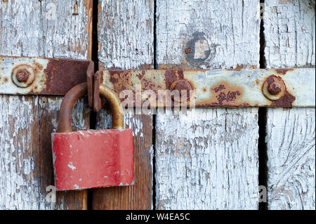 Alte braune Schloss auf einer grauen Tür mit Holzbohlen der Risse im Lack und Rost. Vintage Gates mit Metall Streifen und Schrauben Stockfoto