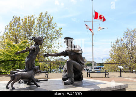 "Die Heimkehr" Statue, direkt am Wasser in der Innenstadt von Victoria, BC an einem sonnigen Tag und an den winken Kanadischen Flagge im Hintergrund. Stockfoto