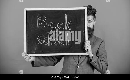 Lehrer oder Schulleiter begrüßt zurück zur Schule. Sind Sie bereit, zu studieren. Lehrer versteckt sich hinter Tafel. Vorbereitung Anfang Schuljahr. Lehrer peeking aus der Tafel über den roten Hintergrund. Stockfoto