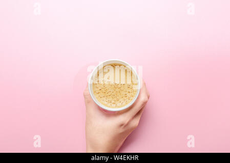 Hand mit einem Styropor Tasse heißen Kaffee über die rosafarbene Tabelle Hintergrund Stockfoto