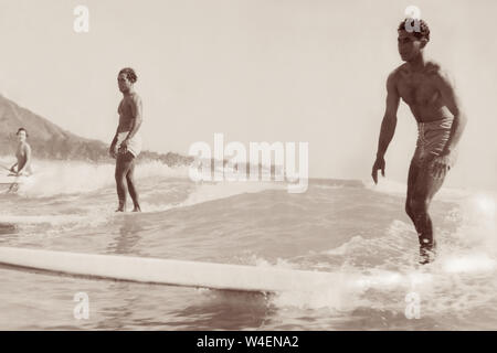 Surfer auf hölzernen Longboards und eine Frau in einem Outrigger Kanu Reiten am Strand von Waikiki in Honolulu, Hawaii, im Frühjahr 1936. Stockfoto