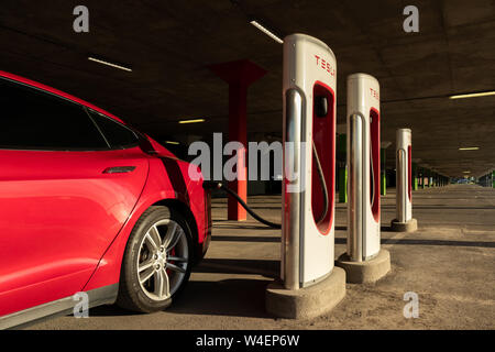 Leuchtendes Rot Tesla Model S Plug-in, das Aufladen in Montreal Tesla Kompressor Lage am Place Vertu Einkaufszentrum während des Sonnenuntergangs. Stockfoto