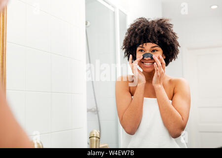 Lächelnde Frau, die Nase Patch. Junge Frau in weißen Handtuch im Bad eingewickelt. Stockfoto
