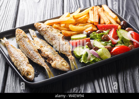 Frisch gebratenen boops boops Fisch mit Sommer Gemüse Salat und Pommes frites Close-up auf einem Teller auf den Tisch. Horizontale Stockfoto