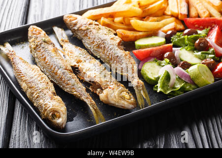 Mediterrane Küche Gebratene boops boops Fisch mit frischem Gemüse Salat und Pommes frites Close-up auf einem Teller auf den Tisch. Horizontale Stockfoto