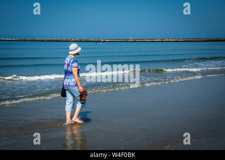 Frau entlang einem Sandstrand mit blauem Himmel und Meer Stockfoto
