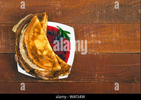 Draufsicht der Pfannkuchen und Marmelade auf einem weißen Teller auf Holztisch. Stockfoto