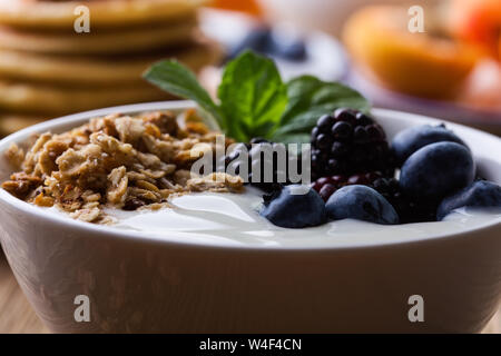 Gesundes Frühstück oder Brunch, Liebling morgen Mahlzeit. Hausgemachtes Müsli mit Joghurt, Pfannkuchen, frischem Sommer Beeren, Früchte, Marmelade auf hölzernen Tisch Stockfoto
