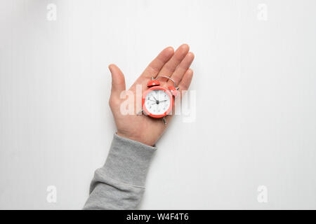 Die Hand eines jungen Mann hält ein roter Wecker. Zeit, Schlaf, Erwachen Konzept. Stockfoto