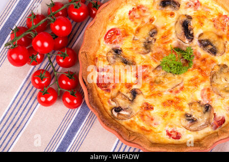 Hausgemachte herzhafte Quiche in Terrakotta Teller auf gestreift Tischdecke mit cherry Strauchtomaten Stockfoto