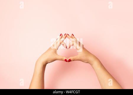 Frauen mit einem roten Hände Maniküre, Herz mit ihren Händen auf rosa Hintergrund. Hand Made in Herzform Liebe Stockfoto