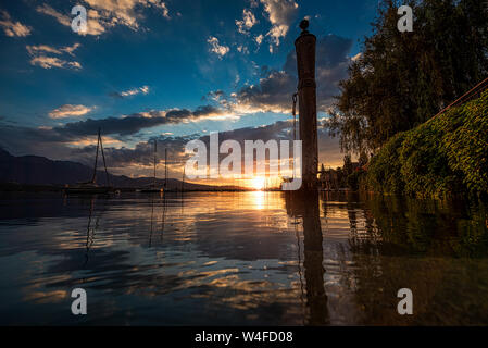 Sonnenuntergang in der Nähe der Wasseroberfläche des Thunersees, einen Liegeplatz Haufen mit Reifen in den Vordergrund und einige Boote am Anker, Bojen Stockfoto