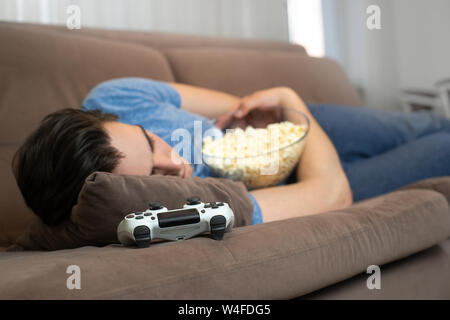 Jungen gutaussehenden Mann einschlafen, nachdem Sie faszinierende video spiel noch Popcorn in seine Hände Stockfoto