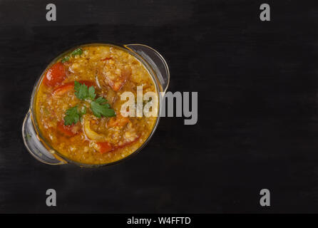 Rote Linsensuppe in einer Glasschale mit Gewürzen, Kräutern, Zwiebeln und Knoblauch auf schwarzem Hintergrund. Flach Stockfoto