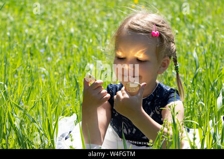 Kleines Mädchen mit einem bitcoin cryptocurrency Münze in Händen. Ein Kind spielt mit Goldmünzen sitzen auf dem Gras Stockfoto