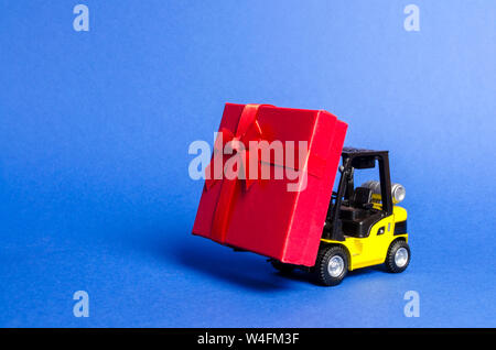 Gelbe Gabelstapler trägt eine rote Geschenkbox mit Schleife. Kauf und Lieferung eines präsentieren. Einzelhandel, Rabatte und Wettbewerbe. Wettbewerb Werbeaktionen. Incre Stockfoto