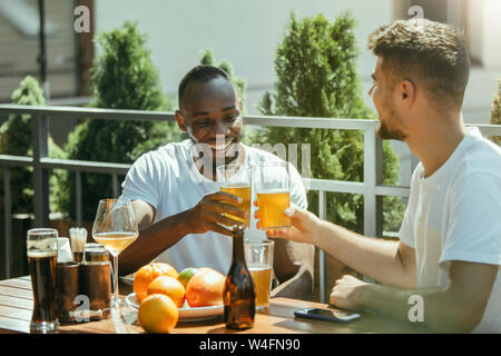 Junge Gruppe von Freunden Bier trinken, Spaß haben und Feiern gemeinsam Laughting. Lächelnde Männer mit Brille's Bier in sonniger Tag. Oktoberfest, Freundschaft, Gemeinsamkeit, Glück, Sommer Konzept. Stockfoto