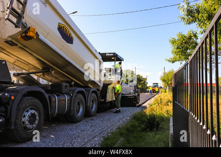 Targoviste, Rumänien - 2019. Arbeitnehmer warten die schwere Muldenkipper frischen und heissen Asphalt mix auf einer vorbereiteten Asphalt fertiger Maschine zu entladen. Bau Stockfoto