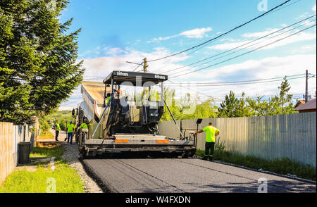 Targoviste, Rumänien - 2019. Arbeitnehmer warten die schwere Muldenkipper frischen und heissen Asphalt mix auf einer vorbereiteten Asphalt fertiger Maschine zu entladen. Bau Stockfoto