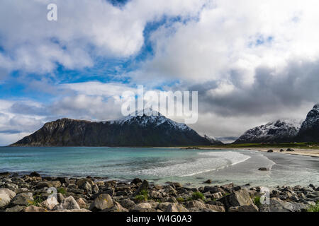 Flakstad Strand, Lofoten, Norwegen an einem schönen Frühlingstag mit einer Prise Schnee auf den umliegenden Hügeln und einem azurblauen Meer Stockfoto