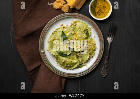 Blick von oben auf die grüne Ravioli in vintage Platte in der Nähe von Silber Gabel schwarzen Holztisch serviert. Stockfoto