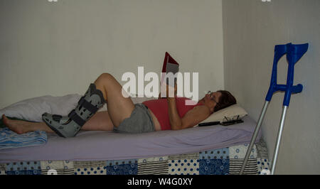 Eine Frau trägt einen Fuß nach Chirurgie liest Ihr Tablet, während im Bett lag, Stockfoto