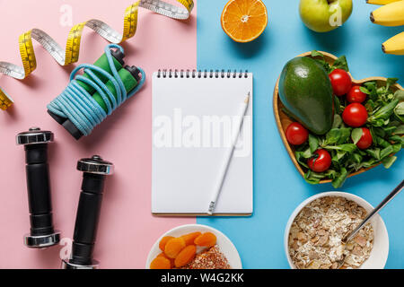 Blick von oben auf die frische Ernährung Lebensmittel in der Nähe von Sport- und Maßband um leer Notebook auf Rosa und blauen Hintergrund Stockfoto