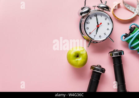 Blick von oben auf die frischen grünen Apfel, Hanteln, Maßband, Springseil und Wecker auf rosa Hintergrund mit Kopie Raum Stockfoto