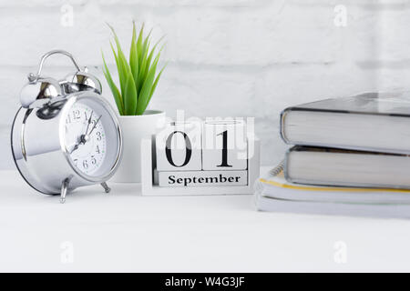 Zurück in der Schule, 1. September auf dem Kalender, Wecker und Schulmaterial auf dem Tisch Stockfoto