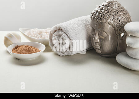 Meersalz und Lehm Pulver in Schalen, Baumwolle Handtuch, Steine, Badebombe und Buddha Figur am weißen Tisch isoliert auf Grau Stockfoto